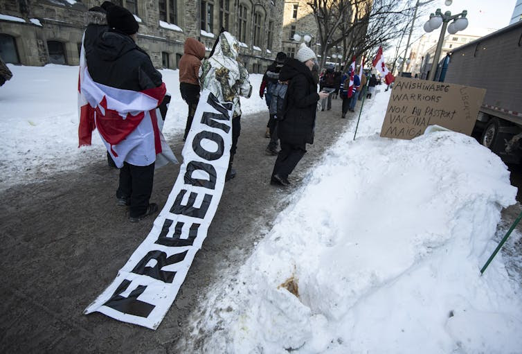 A person walks on a sidewalk as a long banner that reads
          'freedom' trails behind them.