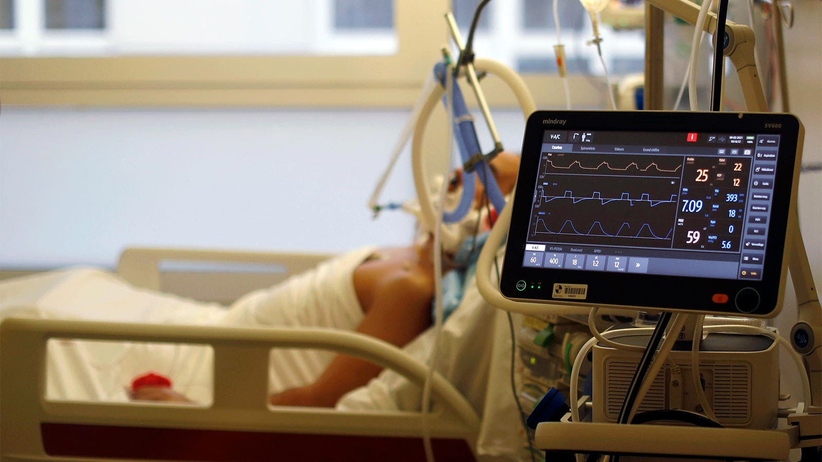 Una foto de un hombre con un ventilador en una cama de hospital en la unidad de cuidados intensivos.