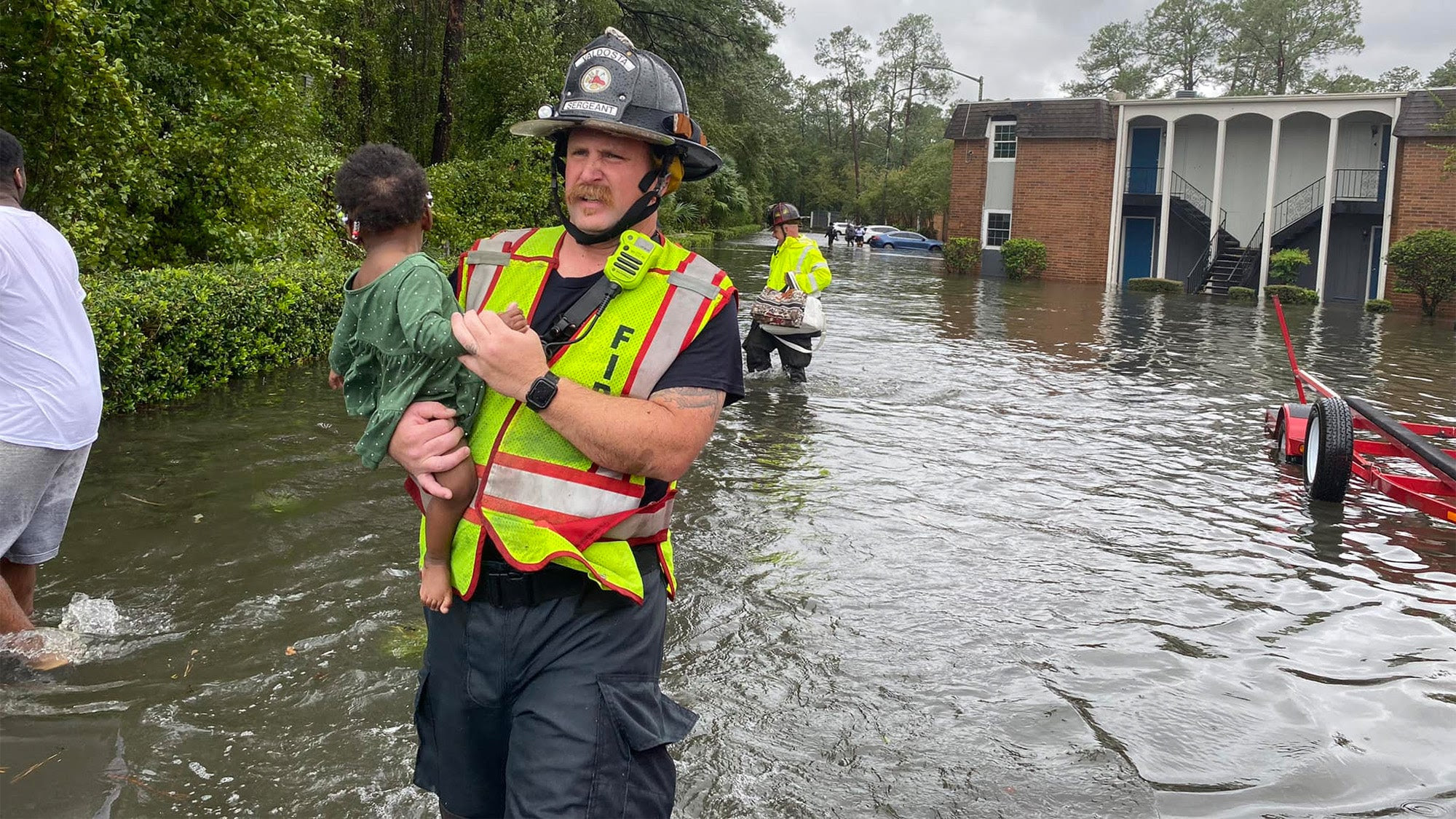 a first responder carries a small child away from flooding.