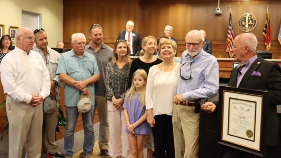 Image of Ray White standing with his family in front of the Board of Commissioner, as Chairman Woodard presents his award.