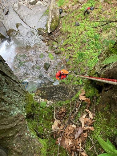 Ranger dangling from ropes near a waterfall during wilderness recovery