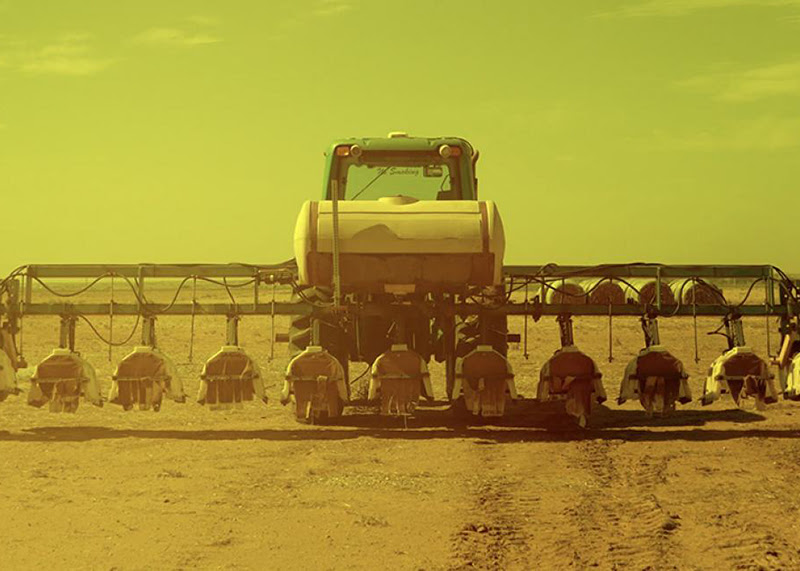 A still from Adam Farcus' 'Solastalgia (Lubbock)'. It shows a combine harvester travelling across a dusty field