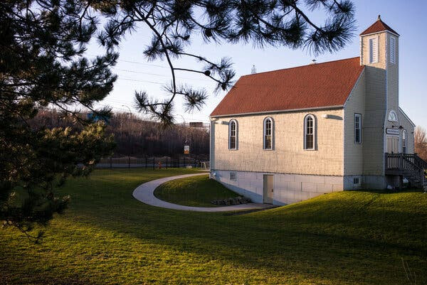 A small, old yellow church with a red roof is now a museum dedicated to the former Black community of Africville outside Nova Scotia. It is in a quiet setting, surrounded by grass.