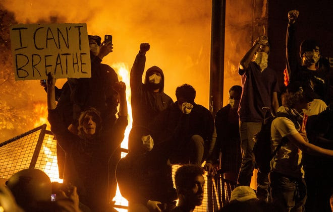 A photo of rioters in masks holding signs as a city burns