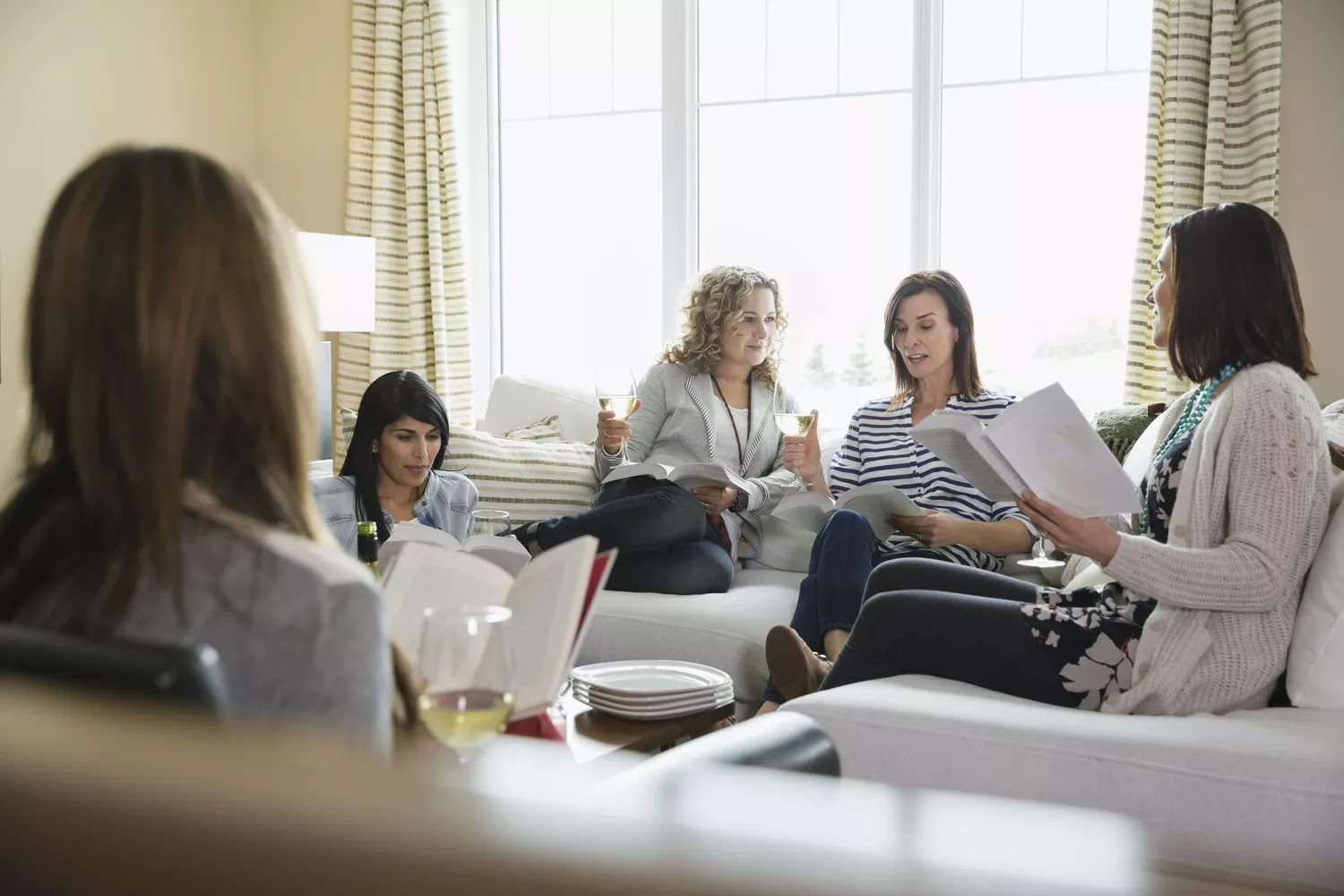 Mature female friends with wineglasses and books at house party