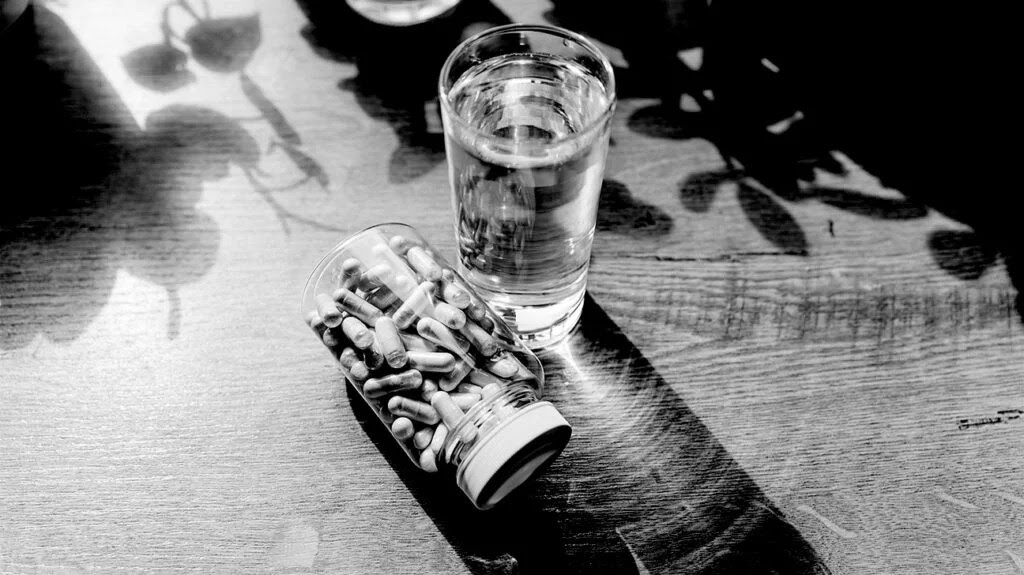 A bottle of supplements on its side next to a glass of water on a flat surface