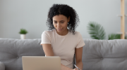 A woman participates in a virtual workshop, taking notes while looking at her computer.