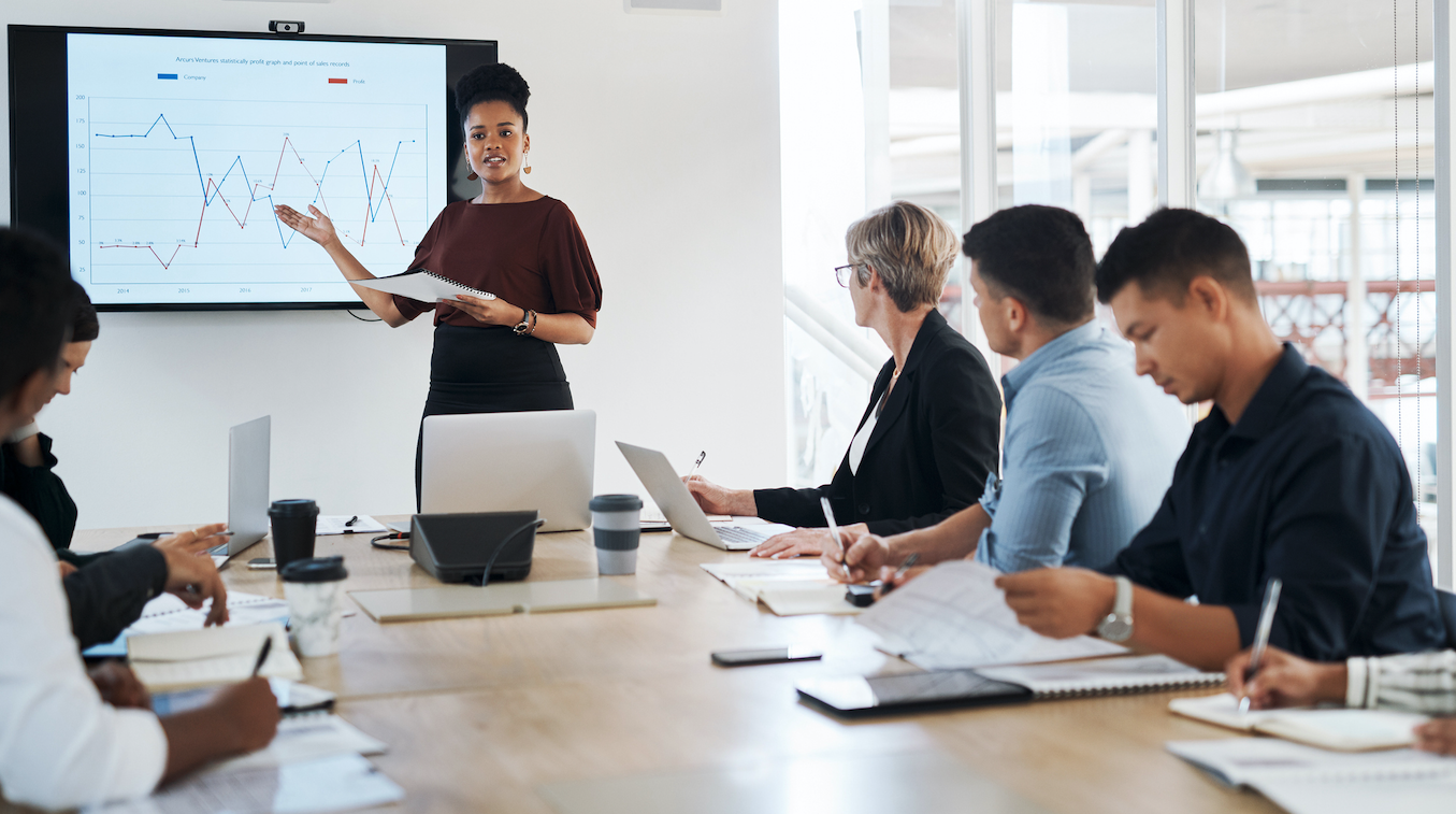 A woman displays data in a presentation as participants take notes.