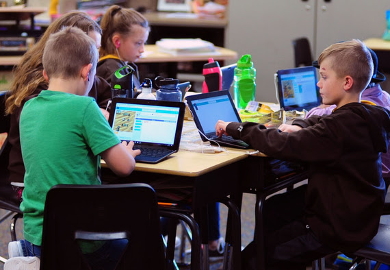 Fourth-grade students sit around a table, each playing a game on a laptop that teaches them to code.