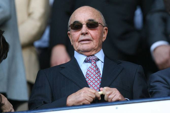 Joe Lewis looking like a Bond villain in tiny little sunglasses and a suit.