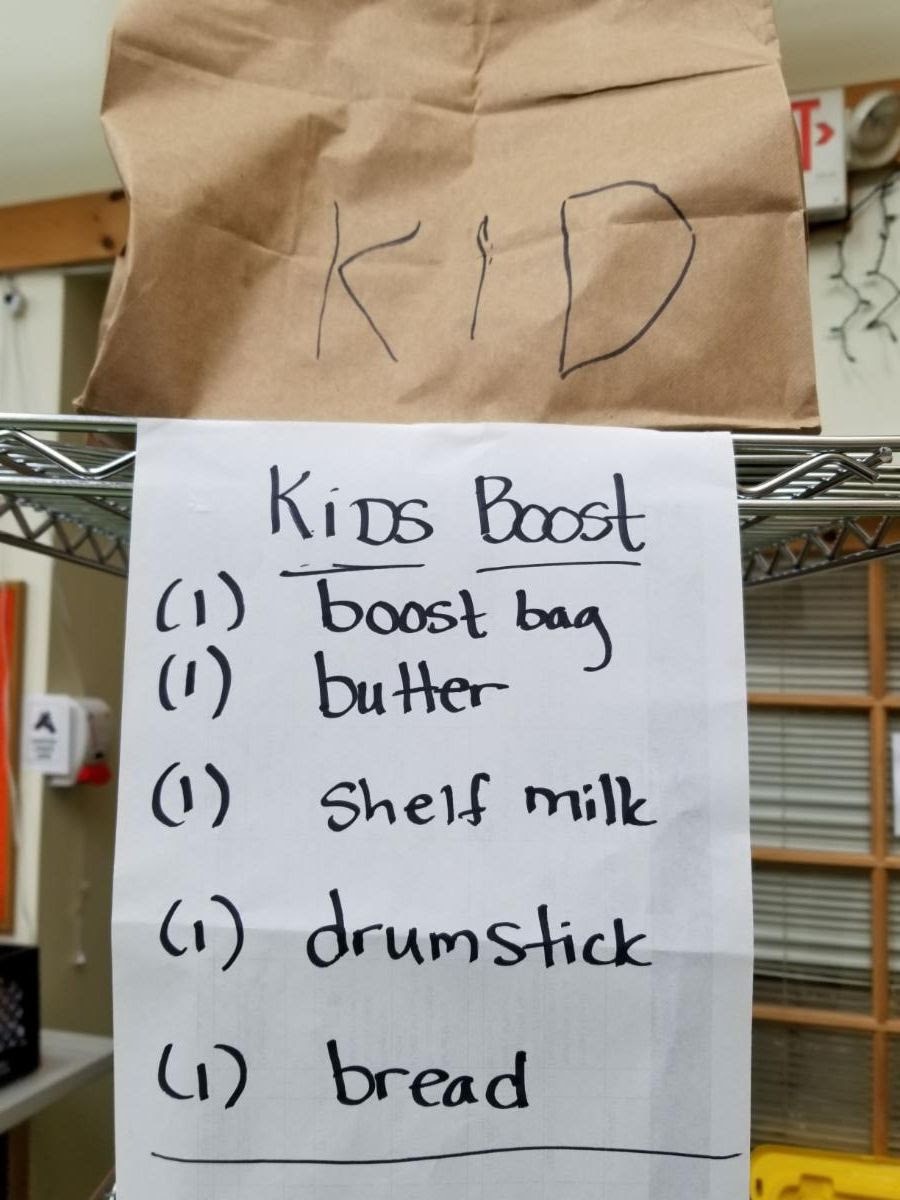Paper grocery bag and sign that reads Kids Boost_ 1 boost bag_ 1 butter_ 1 shelf milk_ 1 drumstick_ 1 bread