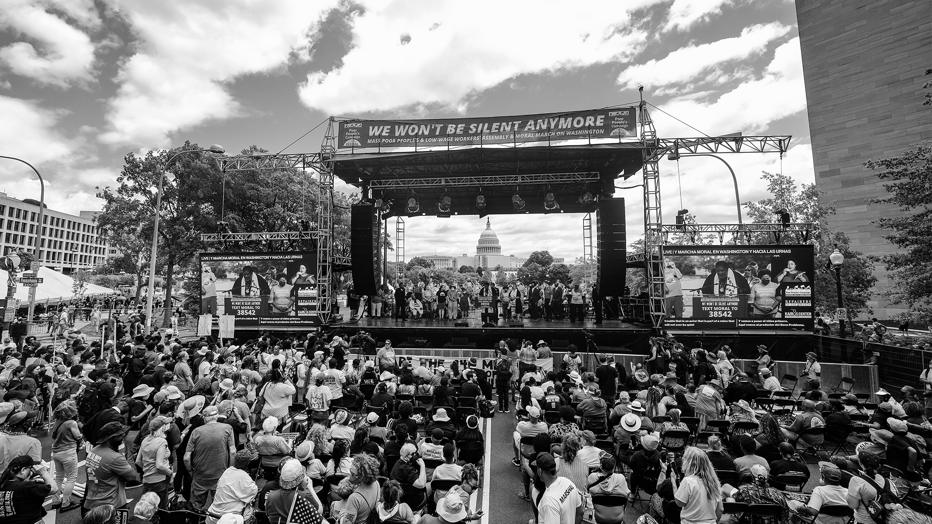 Picture by Steve Pavey from The Mass Poor People’s and Low-Wage Workers’ Assembly and Moral March on Washington and to the Polls . There are thousands of activists looking towards a stage with the Moral Justice Choir. The State Capital Building is in the background.