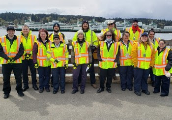 Fourteen people in safety vests with several ferries in the background
