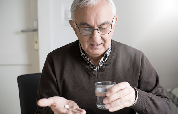 An elderly man holding medicine in his hand.