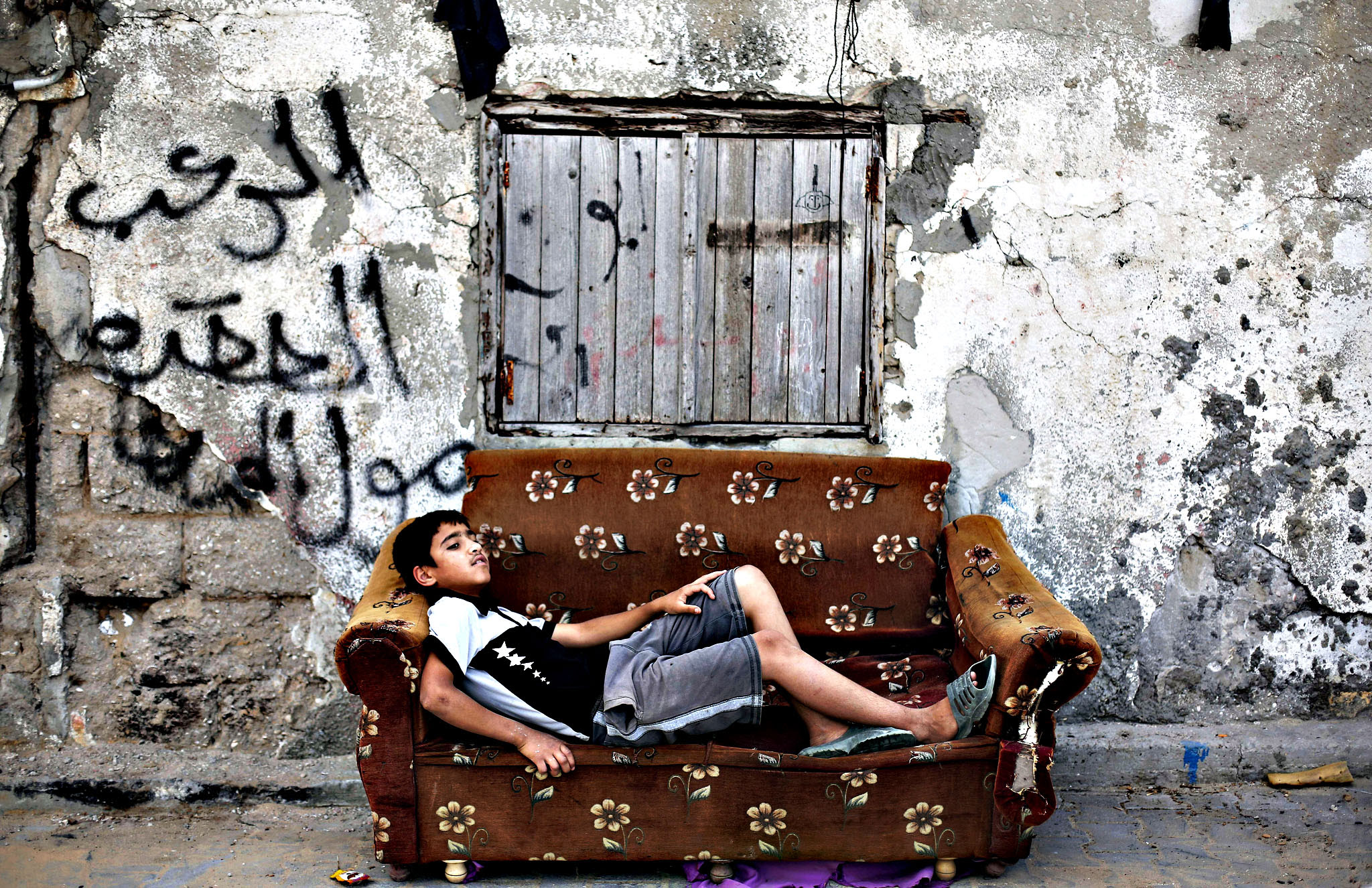 A Palestinian boy rests on an old armcha...A Palestinian boy rests on an old armchair in front of a dilapidated house on May 22, 2015 in Gaza City