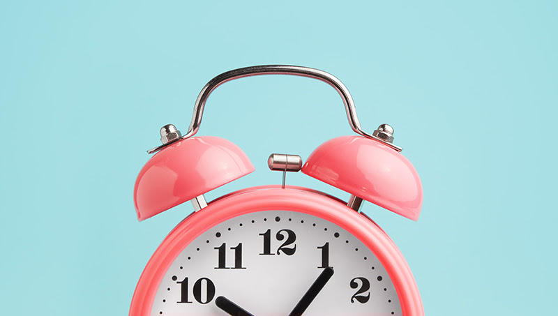 A photo of a pink alarm clock in front of a blue background