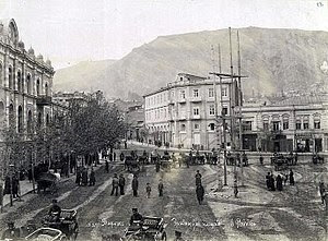 A picture of a city square with people walking about and people riding in carriages