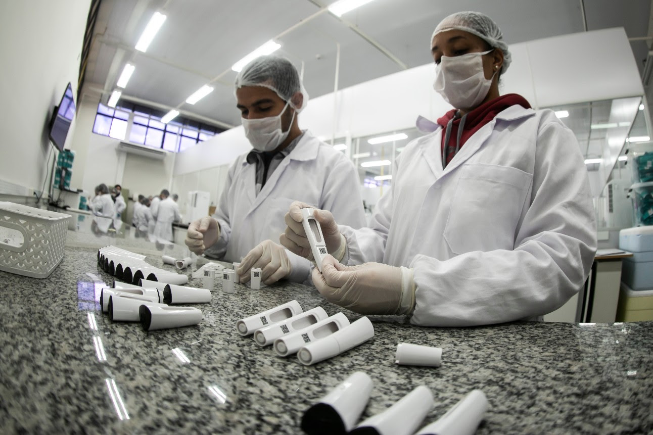 Funcionários de um laboratório, vestidos de jaleco e máscara, manuseiam amostras de sangue de teste rápido de covid-19
