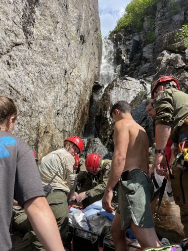 Rangers and hikers helping package up injured hiker near large rockface