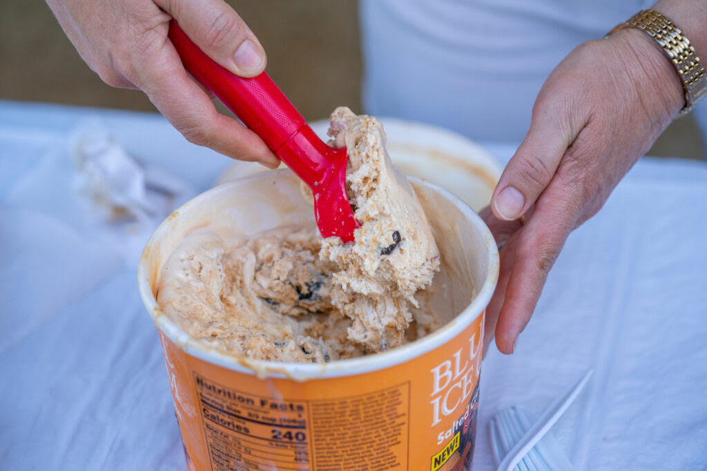 A person scoops ice cream from a half-gallon container.