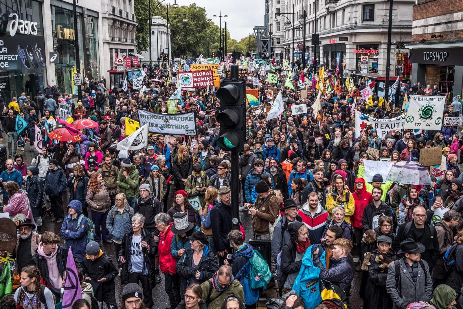 A massive march with thousands of rebels on Oxford Street in London. There are banners which read 'Global Women's Strike' and 'Without Nature We Are Nothing'.