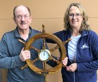 Two people posing for a photo with both of them holding a ship's wheel