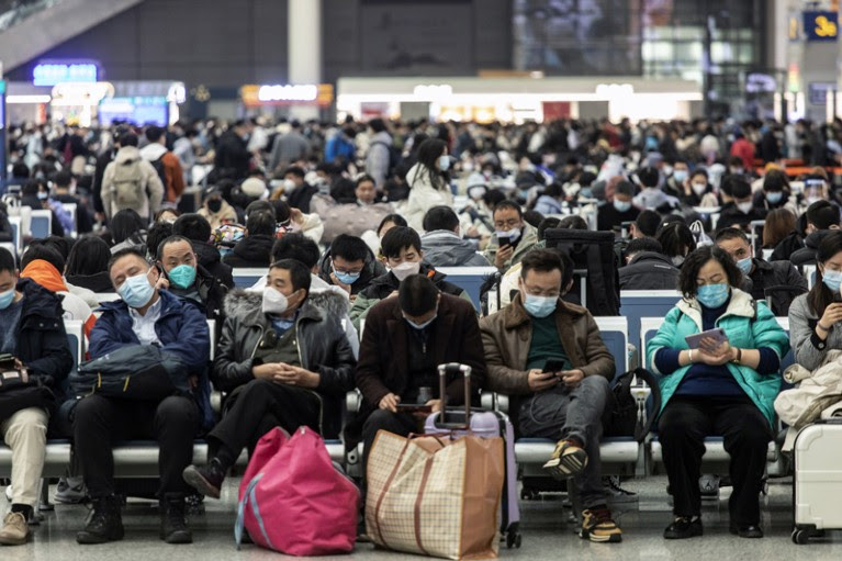 Travellers wearing face masks sit on rows of chairs with their luggage at Shanghai Hongqiao Railway Station