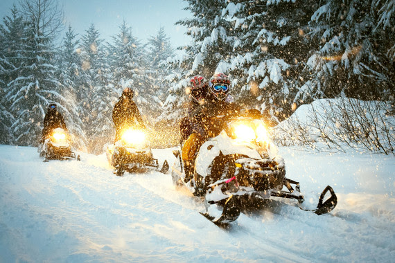 Snowmobiles moving on a snow path at dusk.