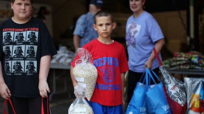 Dois meninos olham para foto, em área de banco de alimentos