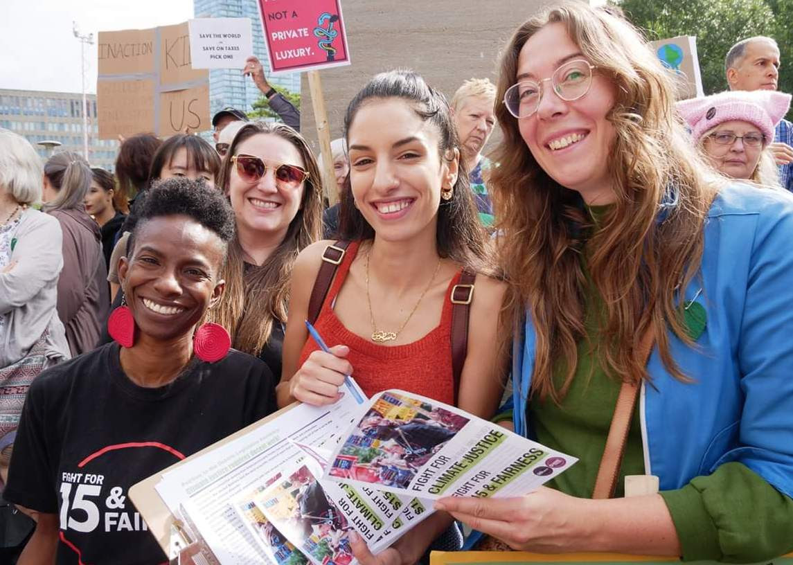 3 women holding $15 & fairness leaflets about climate
justice