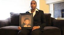 Photo of Shalisa Hayes sitting in a living room holding a photograph of her son