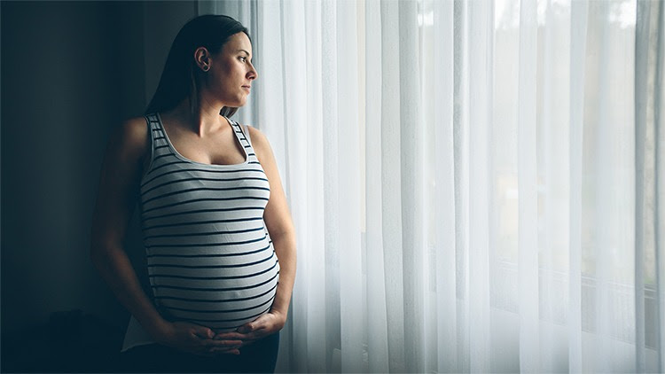 The figure shows a pregnant woman holding her abdomen in front of a curtain while looking outside. 
