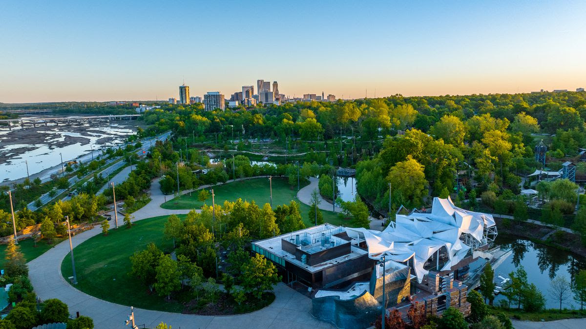 An aerial shot of green trees and park paths, with downtown buildings in the distance.