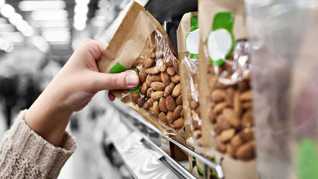 A person picking up almonds at a grocery store.