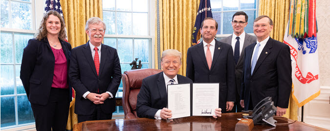 President holding signed copy of National Biodefense Strategy with Secretary Azar, Dr Kadlec, and others standing in background