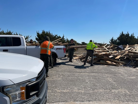 National Park Service employees transfer debris from the back of a truck onto a debris collection pile in the off-road vehicle ramp 23 parking area.