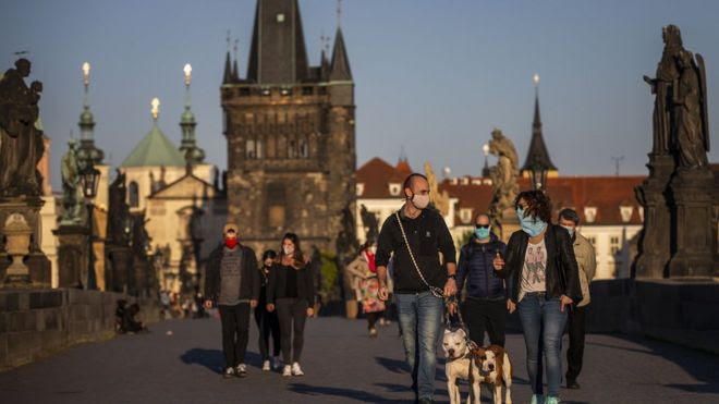 Pedestres de máscara andando em rua história de Praga