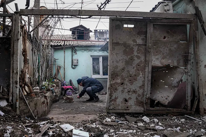 A man lights a fire under a kettle outside a home hit by shelling in Mariupol.