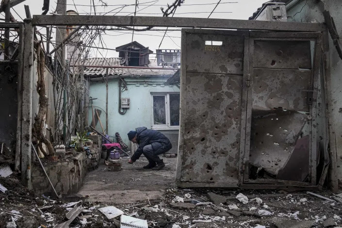 A man lights a fire under a kettle outside a home hit by shelling in Mariupol.