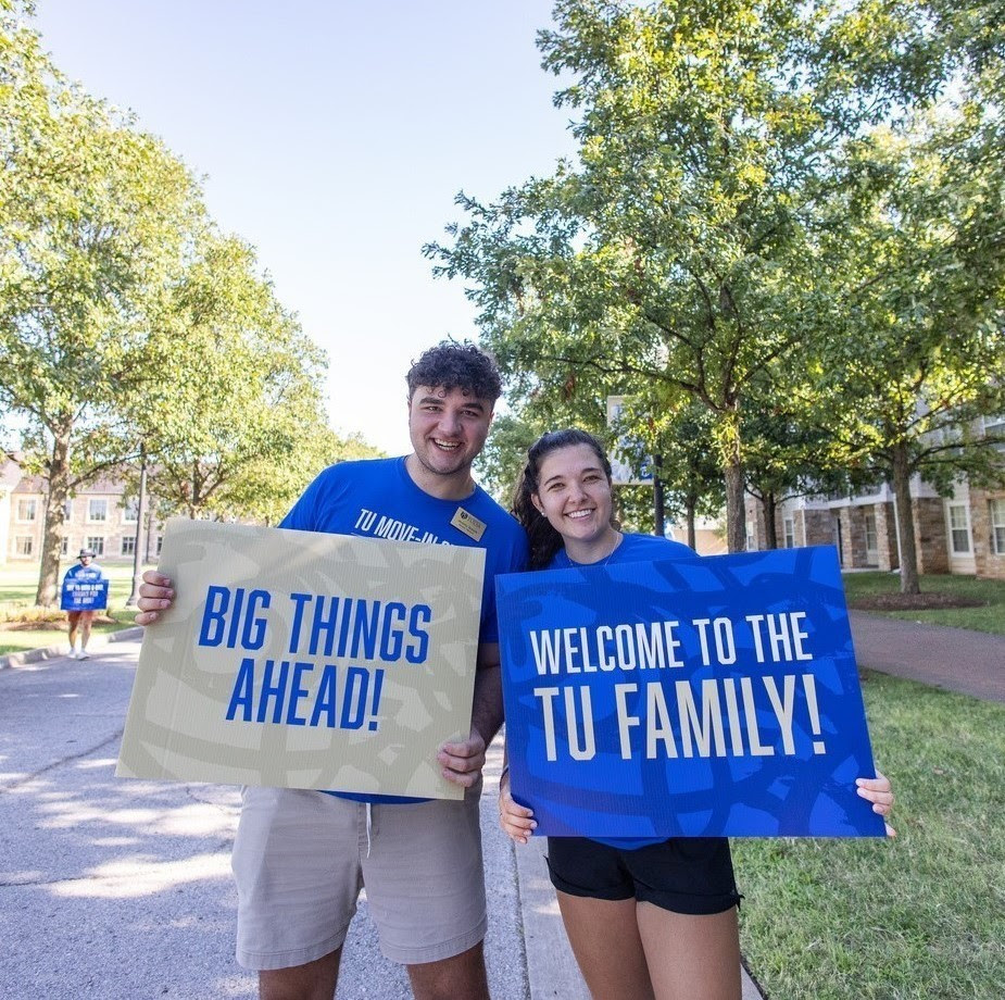 Photograph with two students holding welcome signs to TU.