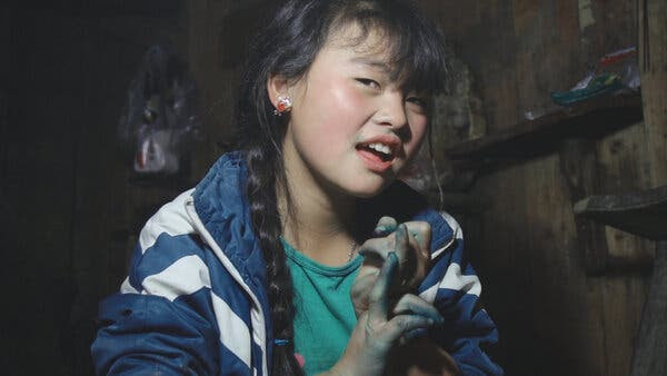 A girl looks at the camera with a half-smile, in a blue jacket and with green paint on her fingers.