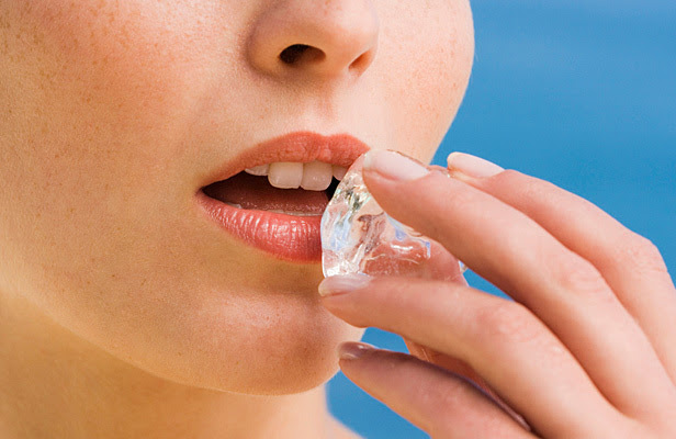 A closeup of a woman applying ice to her mouth.