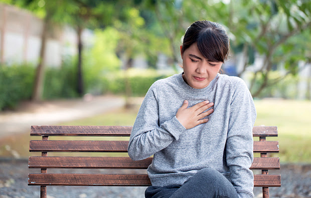A woman sitting on a park bench holding her chest.