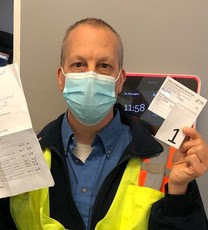 Person wearing mask in TriMet uniform holding immunization card.