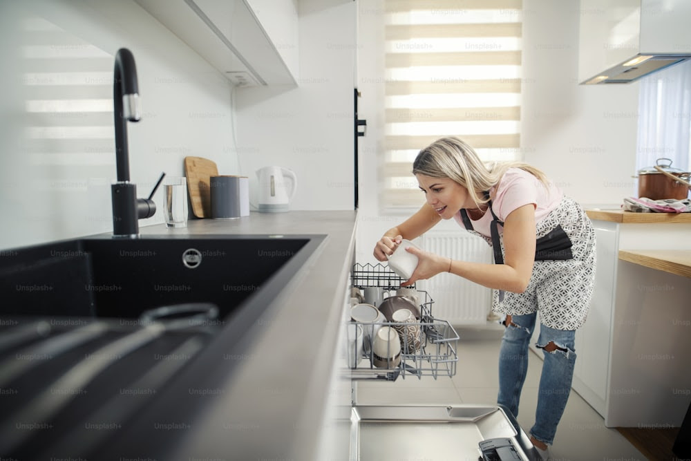 Une femme bien rangée mettant la vaisselle dans un lave-vaisselle dans sa cuisine.