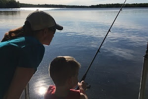 back view of woman and young boy fishing along the shore, bright blue sky