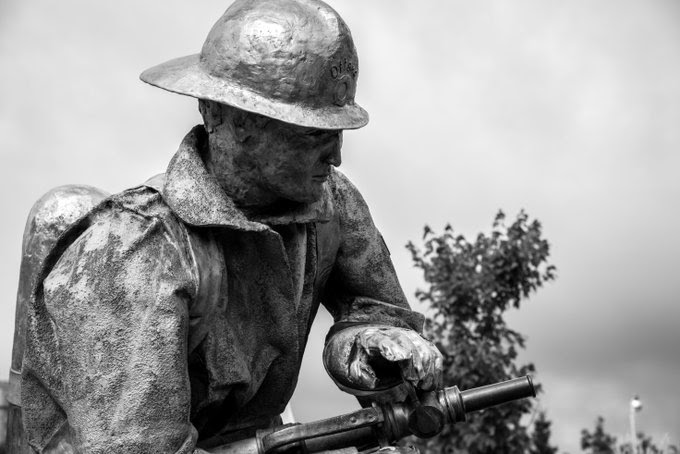 A stone statue of a firefighter holding a water hose.