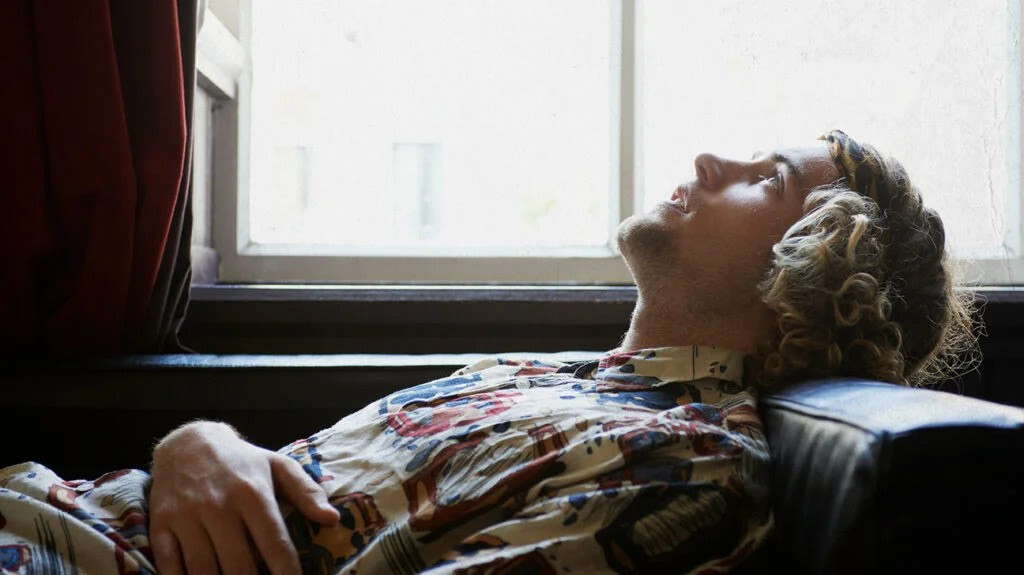 A young person on a comfy chair staring at the ceiling next to a window