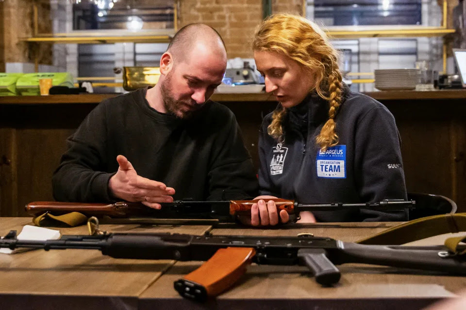 A member of Ukraine&#x002019;s Territorial Defense Forces holds a Kalashnikov rifle as a volunteer looks on.