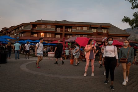 Crowds of people wearing masks walk around a resort town at dusk.
